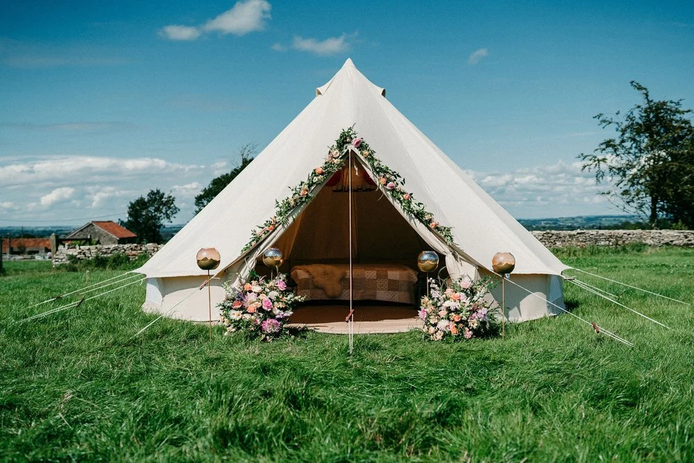 Blank Canvas bell tent dressed with flowers and bunting in a Devon field